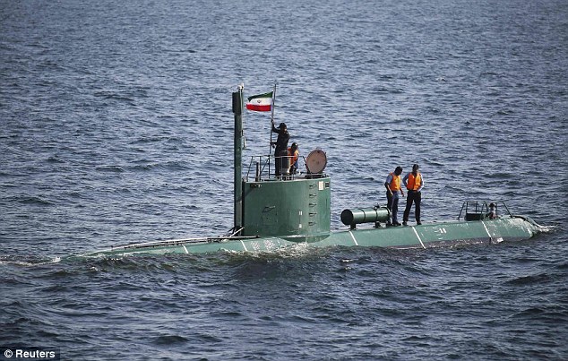 Military personnel place an Iranian flag on a submarine in the Strat of Hormuz, as tensions escalate over the country's apparent design of nuclear weapons